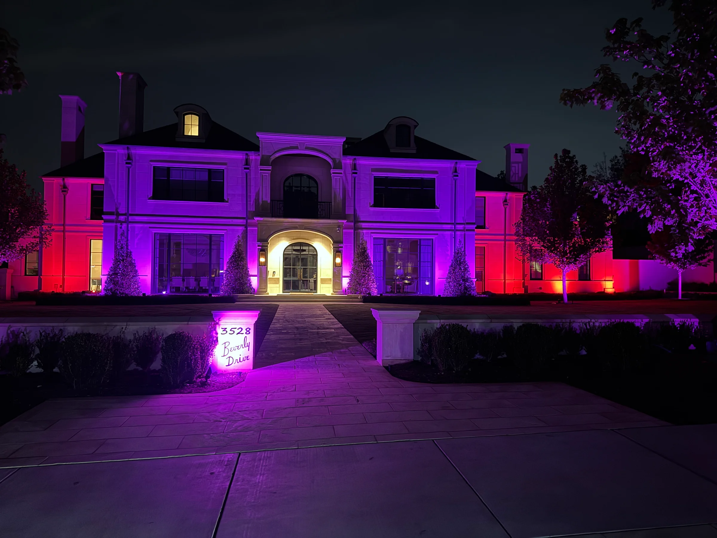 Wide home and mature trees illuminated with vivid multicolor lighting