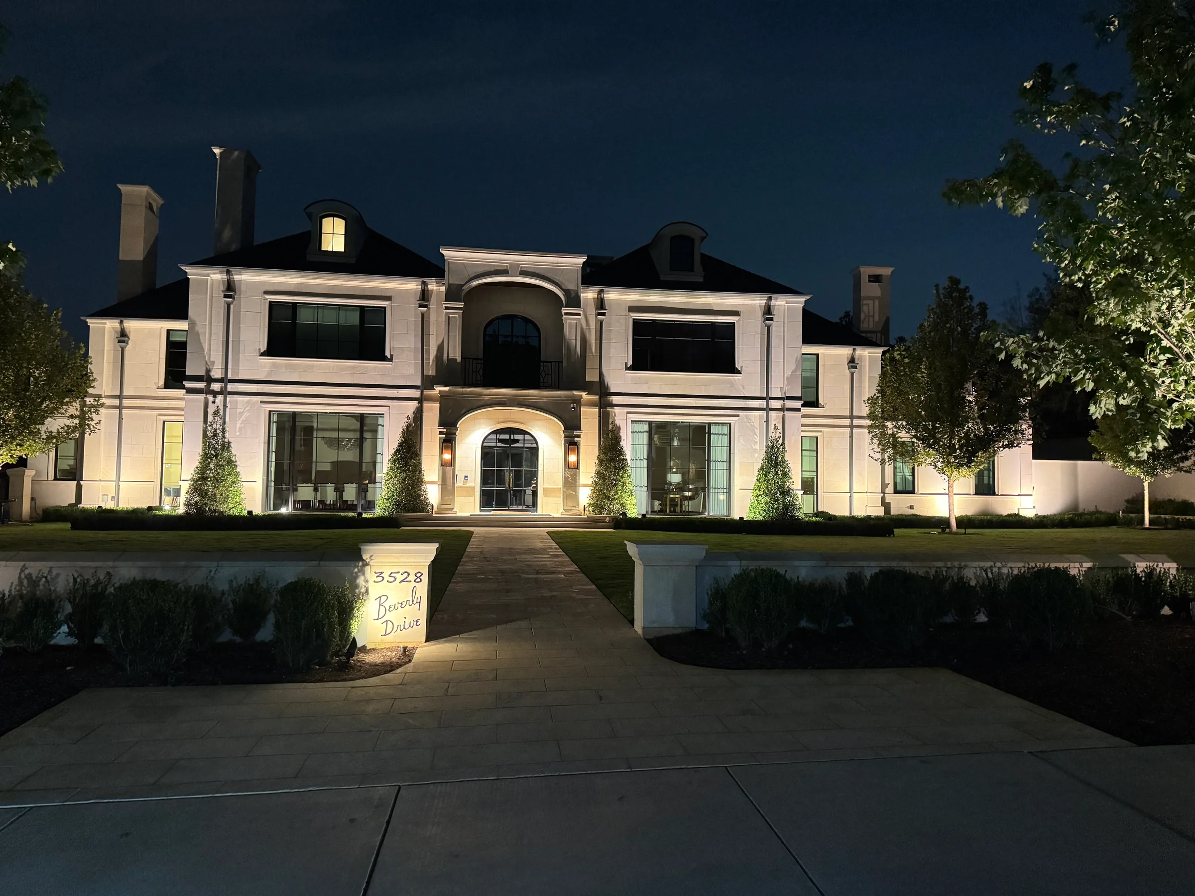 Large stone home illuminated with warm white architectural and tree lighting