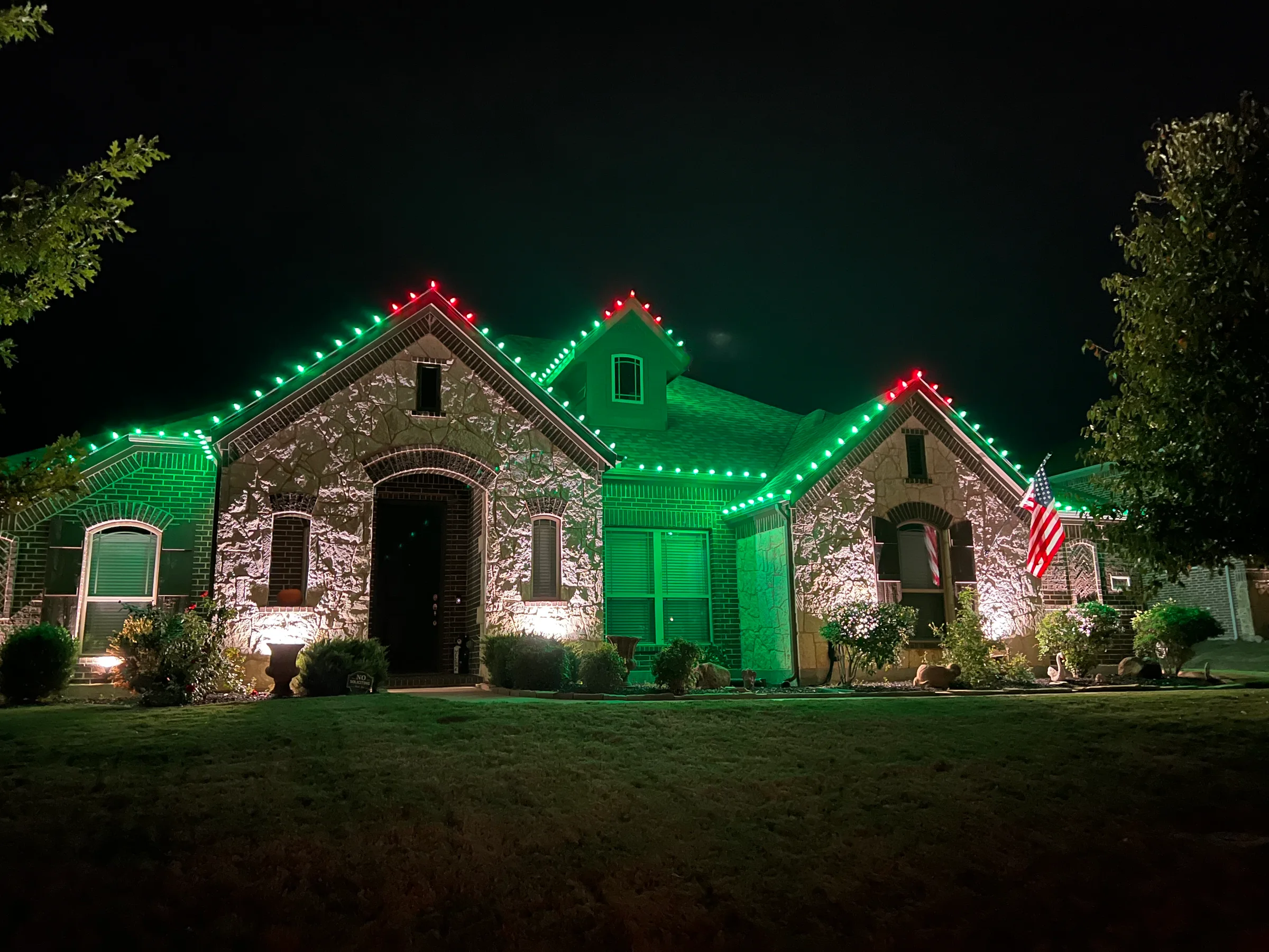 Stone-and-brick home with red and green Christmas lights tracing multiple roof peaks