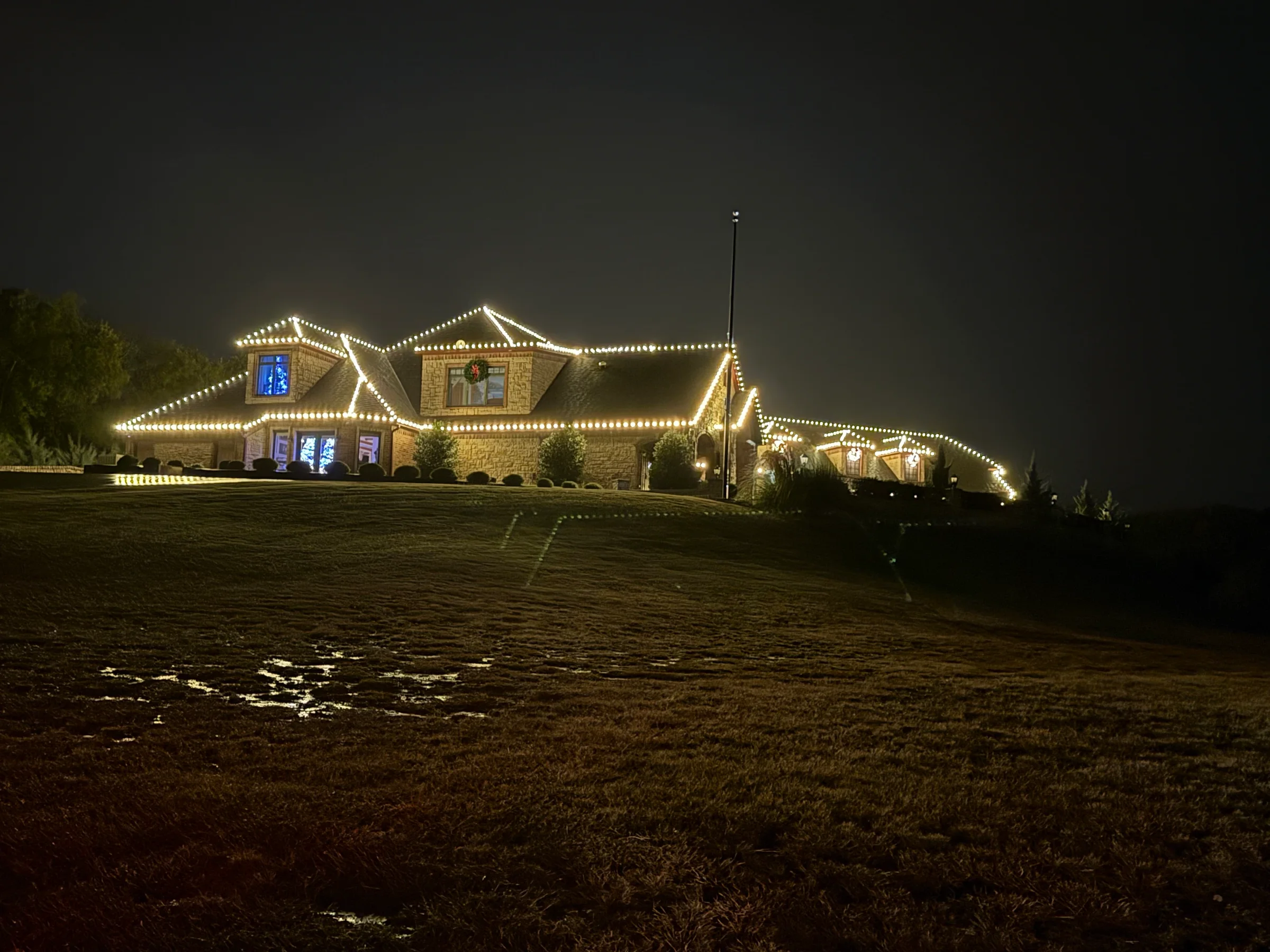 Wide stone home with warm white Christmas lights tracing multiple roof peaks