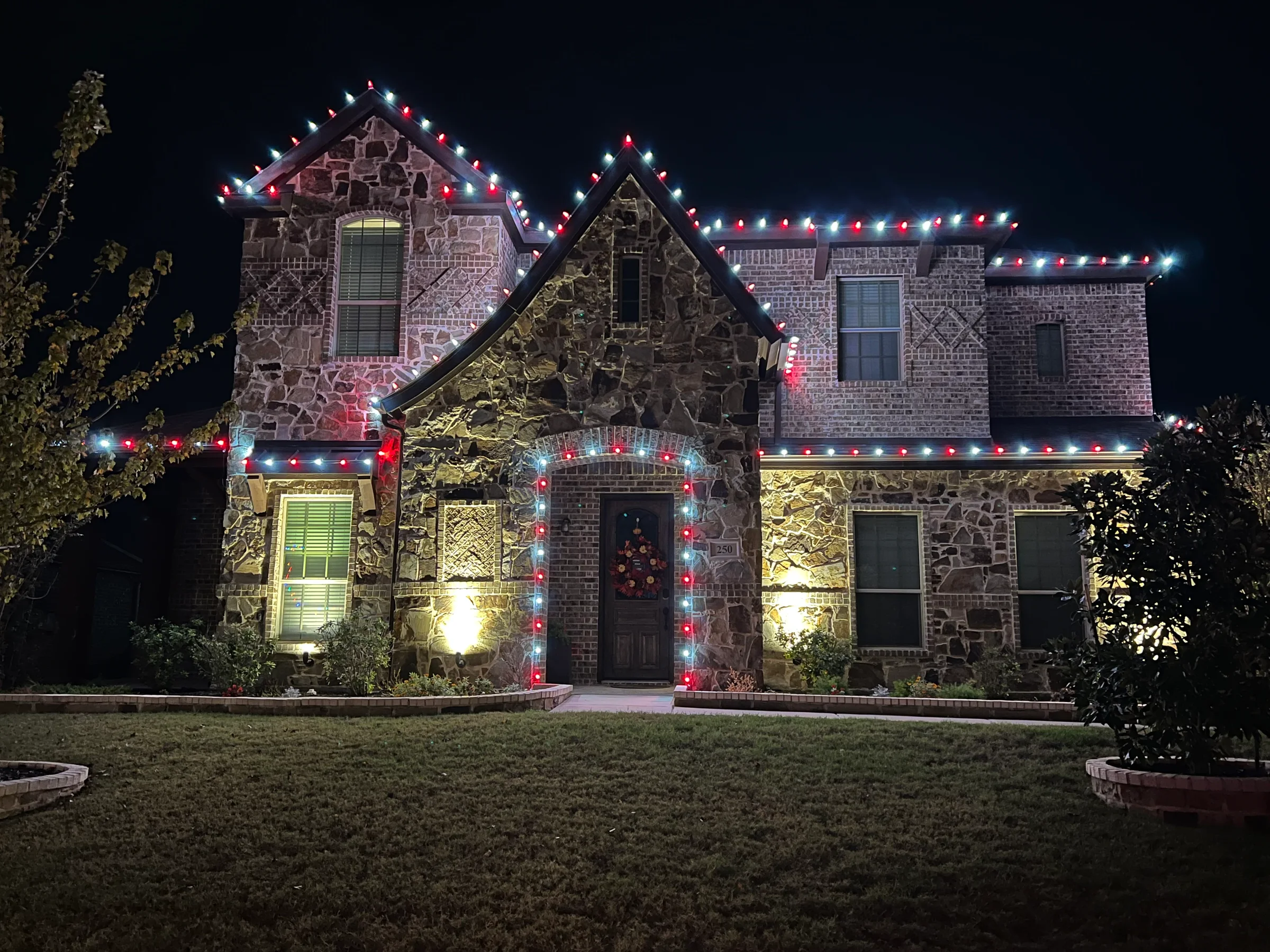 Large two-story stone and brick home outlined with alternating red and cool white Christmas lights