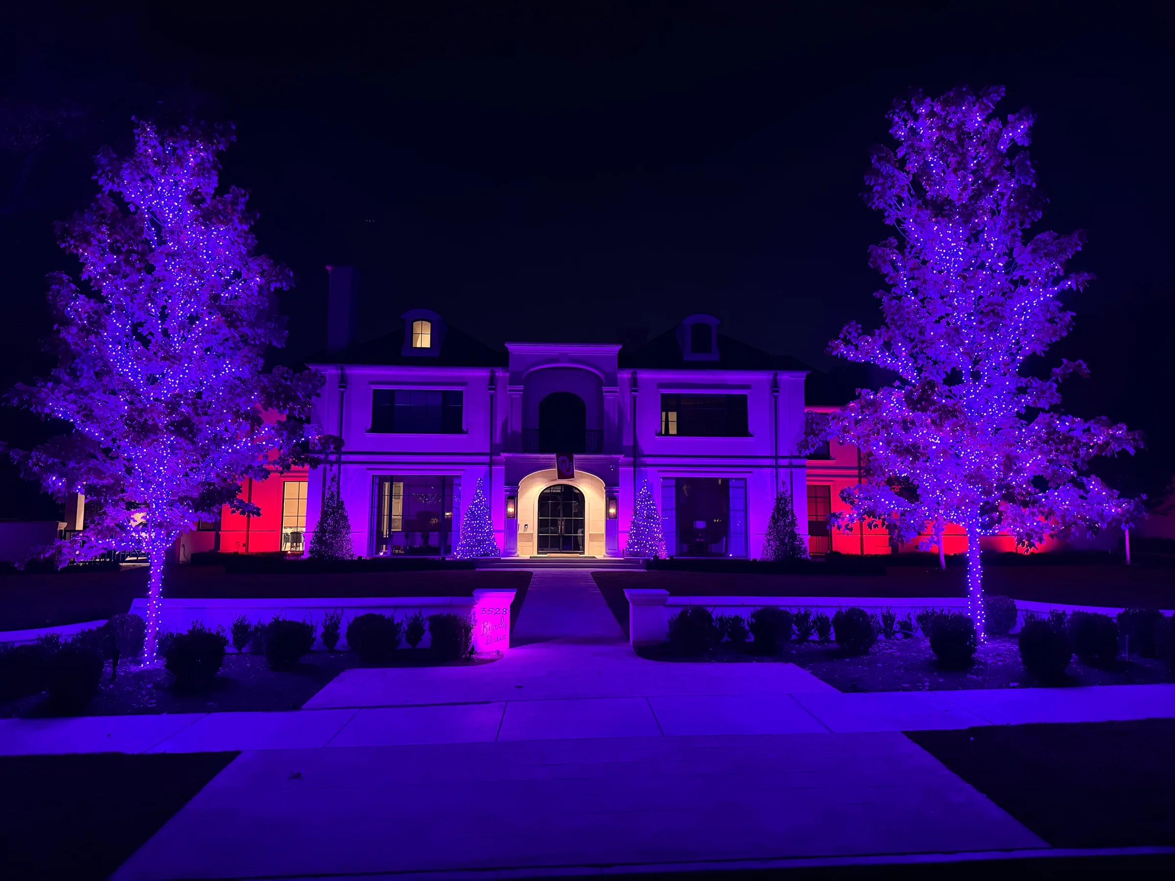 Estate facade and two front trees illuminated in purple and magenta