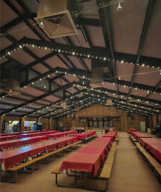 Covered event hall with warm white string lights running across exposed ceiling beams above rows of tables