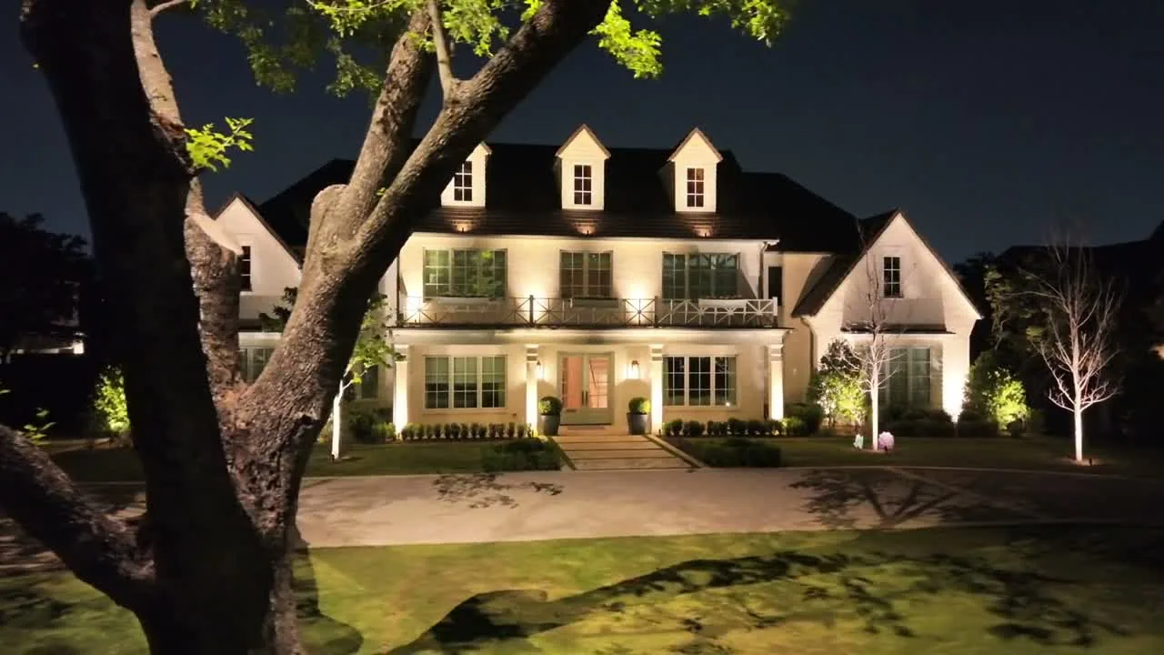 Two-story home, mature front tree, and landscaping illuminated with warm white light