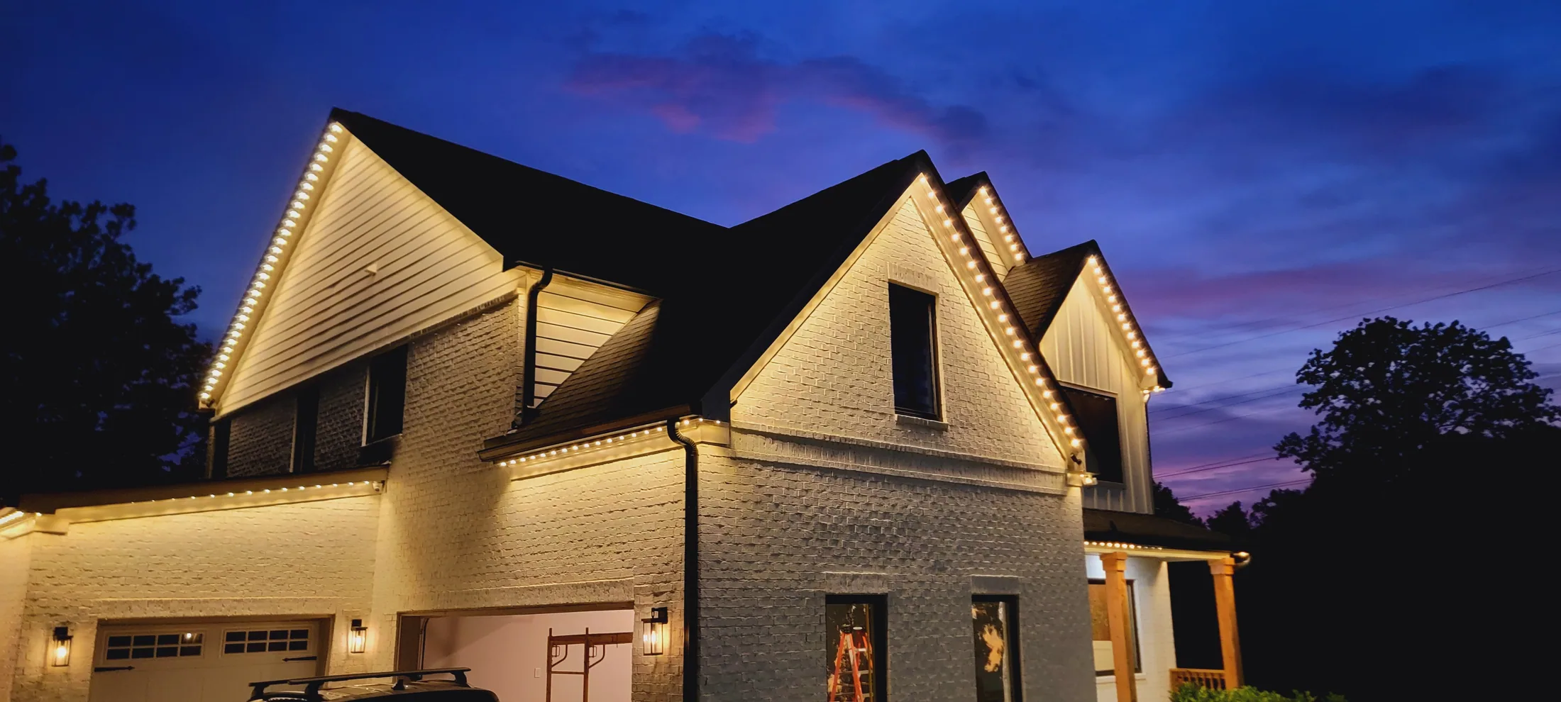 Warm white permanent lighting outlining a two-story home at dusk